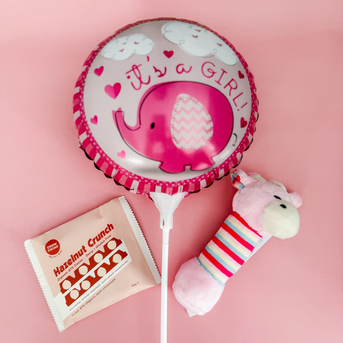 Pink balloon with elephant design, Hazelnut Crunch packet, and plush rattle on pink background | Flowers & Gift Delivery Perth