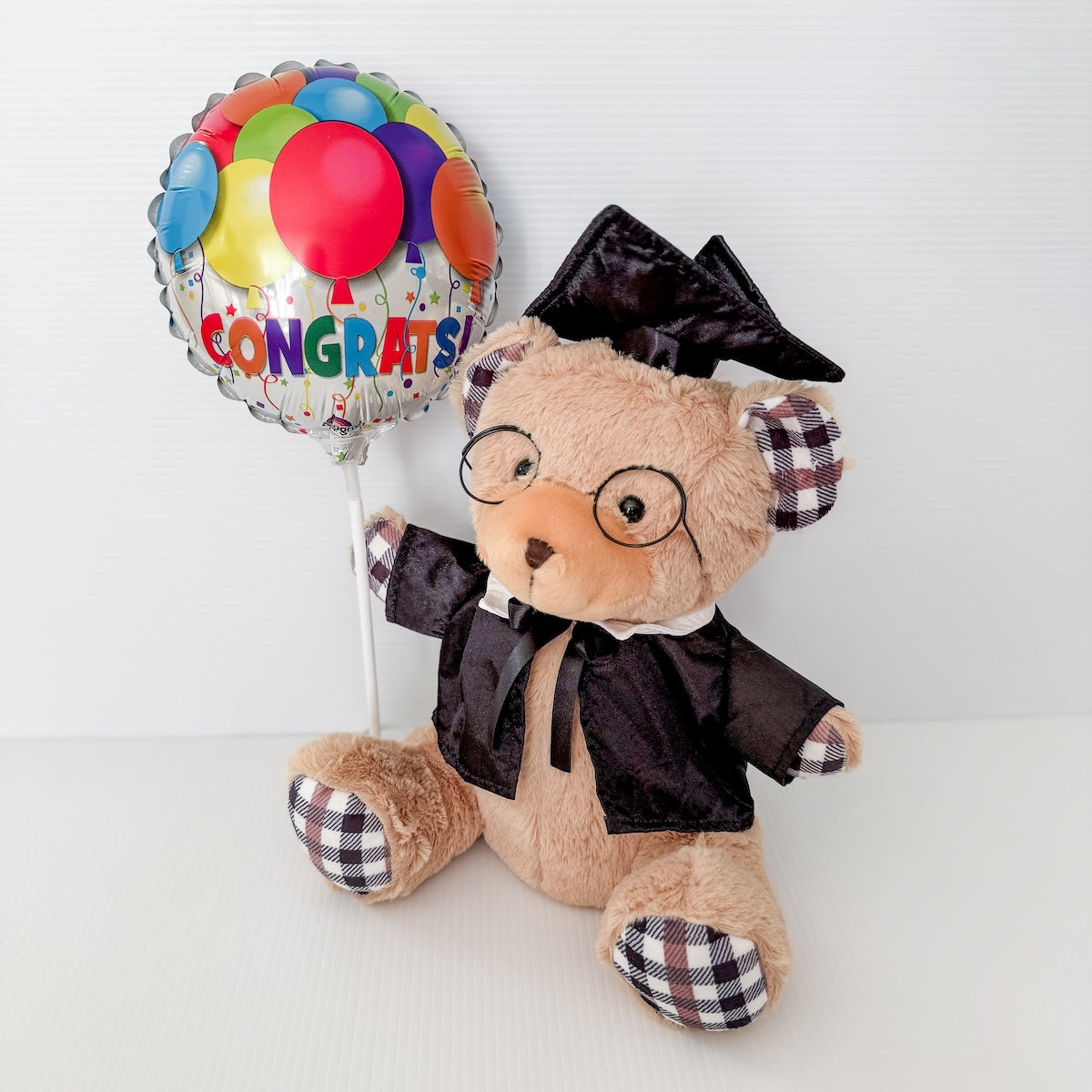 Graduation-themed teddy bear with a 'Congrats' balloon on a white background