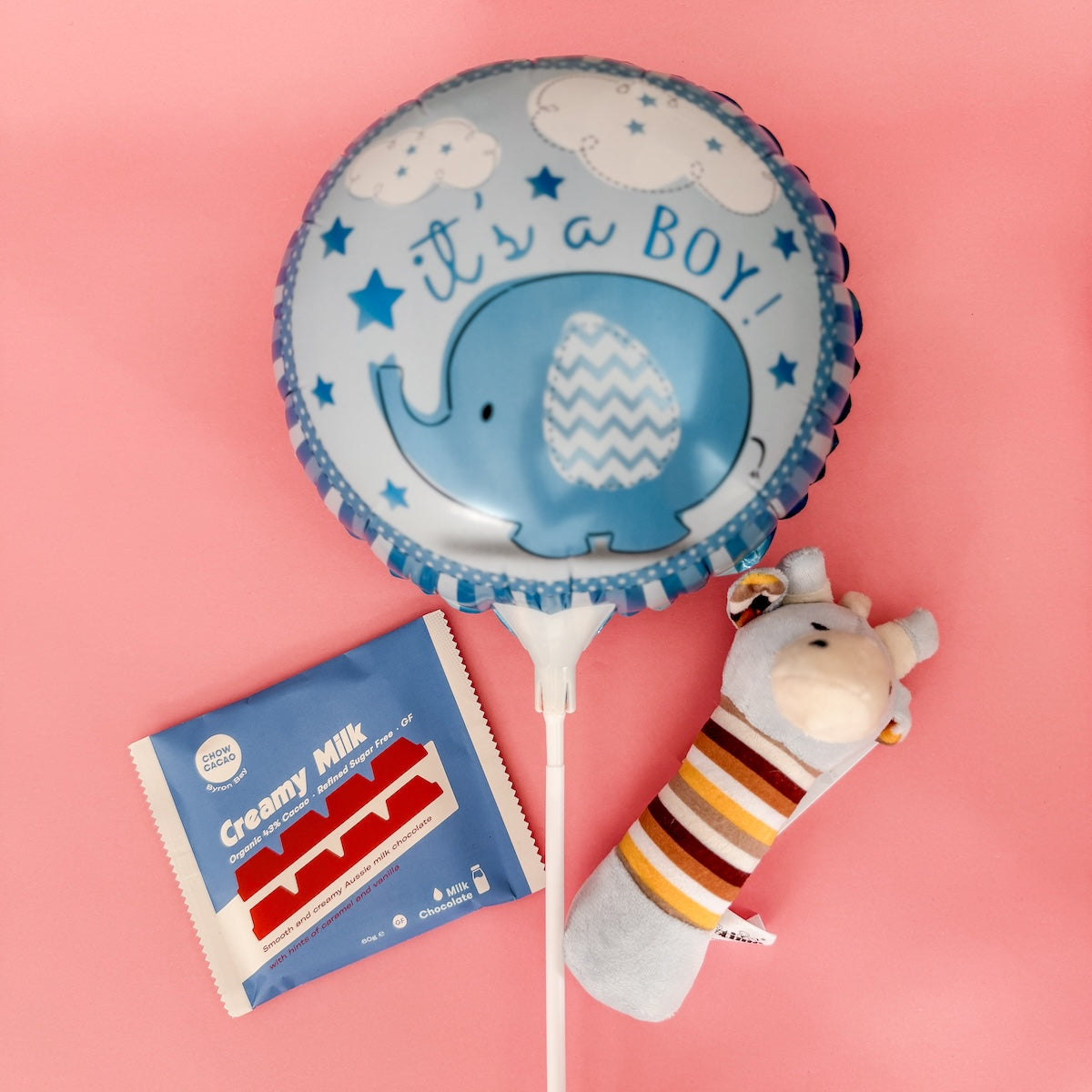 Blue balloon with elephant design and 'it's a boy!' text, next to a packet of Creamy Milk and a small plush rattle | Gift & Flower Delivery Perth
