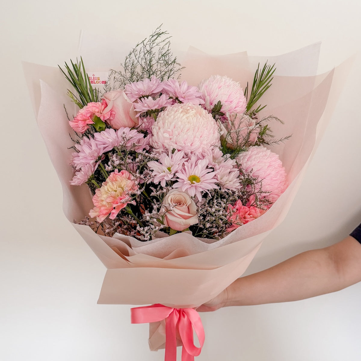 A bouquet of soft and vibrant pink blooms wrapped in pink non-woven paper with a pink ribbon.