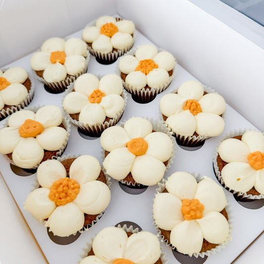 Carrot cupcakes decorated like flowers with white frosting and orange centres on a white box. Baked by The Good Carrot for Bliss and Bloom Studio, Perth Florist.